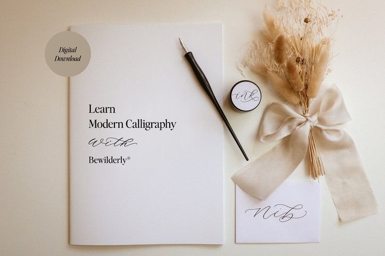 May include: A white booklet with the text "Learn Modern Calligraphy with Bewilderly" on the cover. A black calligraphy pen, a small jar of ink, and a piece of paper with the word "nib" written in calligraphy are also shown. The image has a rustic aesthetic with dried flowers and a beige ribbon.