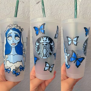 May include: Three clear plastic cups with blue and white designs. The cups feature a character from the movie "The Nightmare Before Christmas", a skull and crossbones, and butterflies. The cups are decorated with blue and white paint.