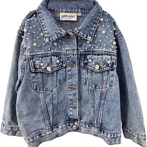 Może przedstawiać: Jasnoniebieska kurtka dżinsowa z perłami. Kurtka ma klasyczny kołnierz, zapięcie na guziki, dwie kieszenie na piersi i dwie kieszenie boczne. Etykieta zawiera nazwę marki "gemma fosati".