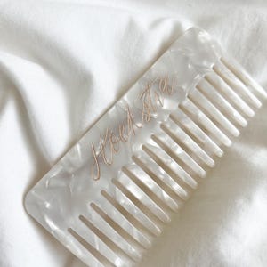Puede incluir: Un peine blanco marmoleado con el nombre "Lorena" inscrito en letras doradas.