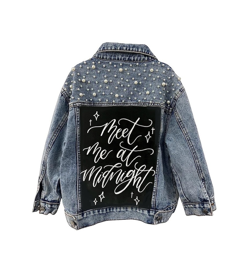 Może przedstawiać: Jasnoniebieska kurtka dżinsowa z perłowymi zdobieniami na ramionach. Z tyłu czarna naszywka z białym napisem "Meet me at Midnight" w ozdobnej czcionce. Kurtka ma klasyczny kołnierz i zapięcia na guziki.