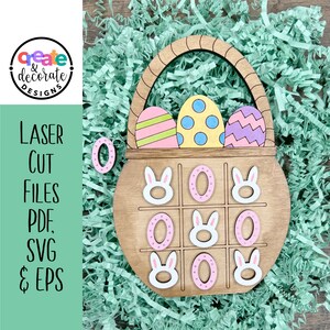 May include: Wooden Easter basket game with a tic-tac-toe board. The board has bunny faces and pink eggs. The basket has three colorful eggs inside.