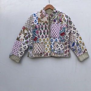 Puede incluir: Una chaqueta acolchada blanca con un diseño de patchwork floral. La chaqueta tiene una cremallera y un cuello mandarín.