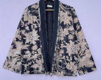 Könnte beinhalten: Eine Jacke mit schwarzem und beigem Blumenmuster und dunkelgrüner Bordüre, die an einem Holzbügel hängt. Die Jacke hat ein lockeres, offenes Design und scheint aus einem gesteppten Stoff zu bestehen. Das Blumenmuster ist detailliert und bedeckt die gesamte Jacke.