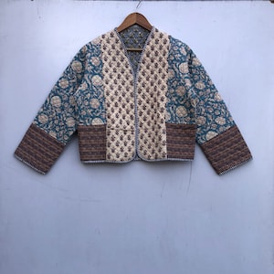 Könnte beinhalten: Eine gesteppte Jacke mit Patchwork-Design in braunen, blauen und cremefarbenen Blumenmustern. Die Jacke hat einen V-Ausschnitt und einen Knopfverschluss.