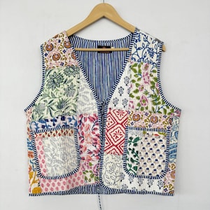 Könnte beinhalten: Eine Patchwork-Weste mit einem blau-weiß gestreiften Futter. Die Weste ist aus Baumwolle und hat einen Bindeverschluss am Hals. Die Weste ist mit verschiedenen Blumenmustern in Rosa-, Grün- und Blautönen verziert.