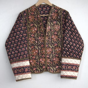 Könnte beinhalten: Eine gesteppte Jacke mit einem Blumendruck in den Farben Rosa, Braun und Grün. Die Jacke hat einen V-Ausschnitt und lange Ärmel mit einem kontrastierenden Besatz.