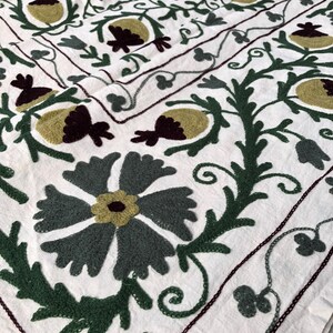May include: White cotton fabric with a green, brown, and white embroidered floral pattern. The design features stylized flowers and leaves.