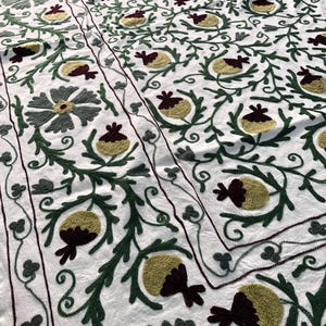 May include: White cotton fabric with a repeating pattern of green, burgundy, and yellow embroidered flowers and leaves.