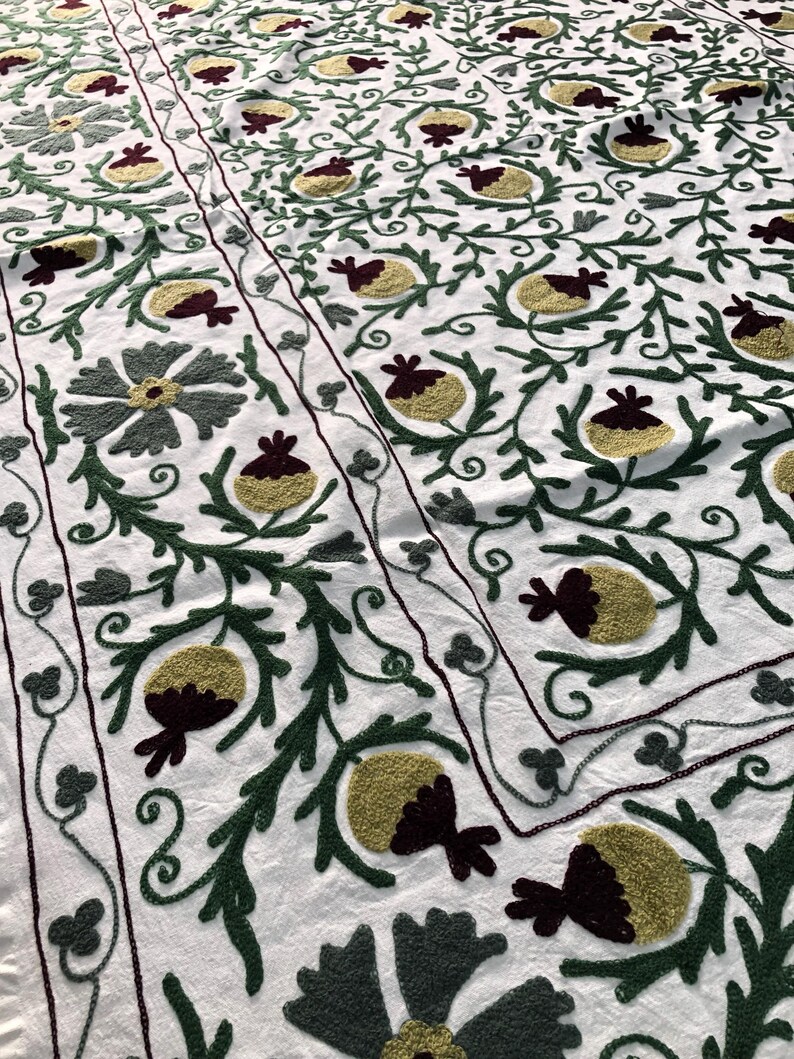 May include: White cotton fabric with a repeating pattern of green, burgundy, and yellow embroidered flowers and leaves.