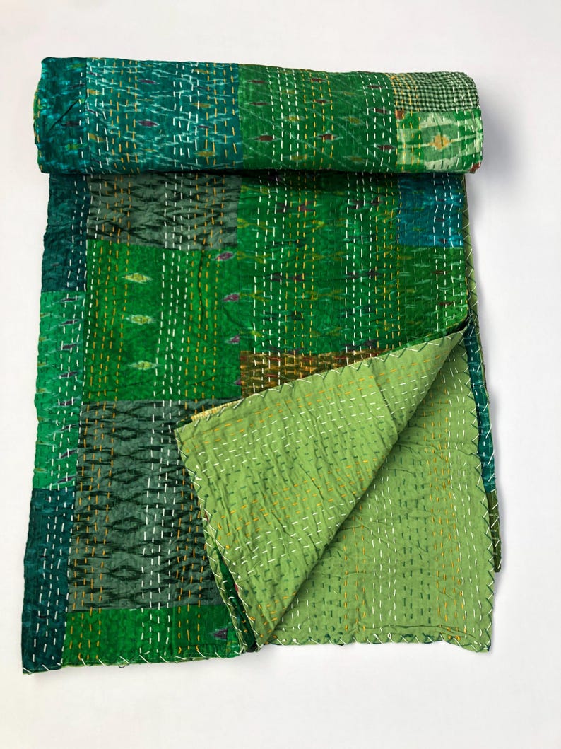May include: A green kantha quilt with a patchwork design. The quilt is made of recycled saris and is hand-stitched. It is a traditional Indian textile.