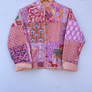 Op de afbeelding: Een roze gewatteerd jack met een patchwork-ontwerp met bloemen- en paisleypatronen. Het jack heeft een mandarijnskraag en lange mouwen met gestreepte manchetten.