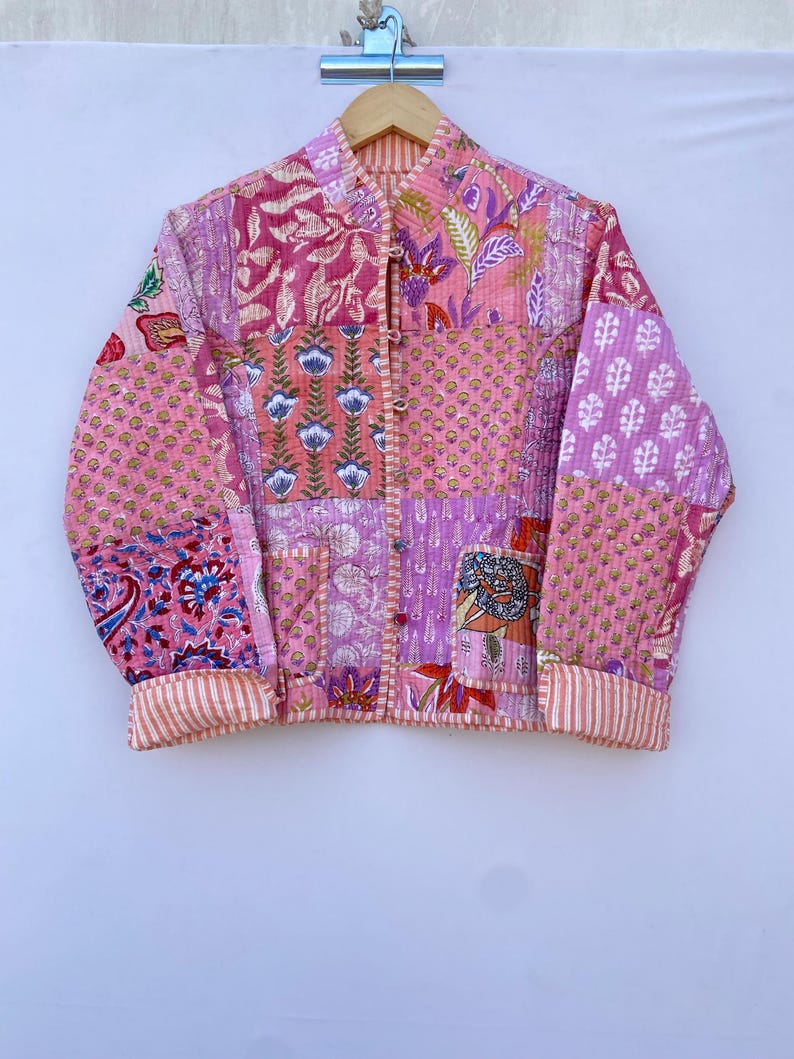 Op de afbeelding: Een roze gewatteerd jack met een patchwork-ontwerp met bloemen- en paisleypatronen. Het jack heeft een mandarijnskraag en lange mouwen met gestreepte manchetten.