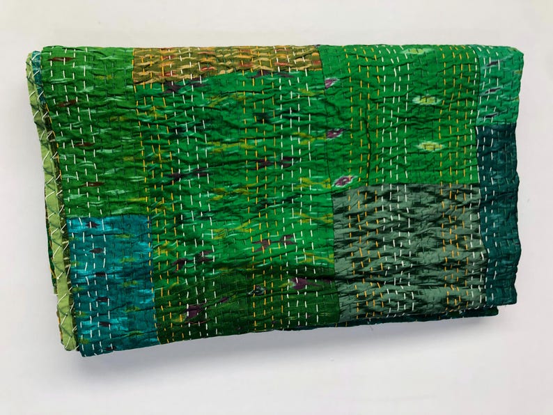 May include: A green kantha quilt with a patchwork design. The quilt is made of recycled saris and is hand-stitched. It has a soft, textured feel and is perfect for adding a touch of bohemian style to your home.
