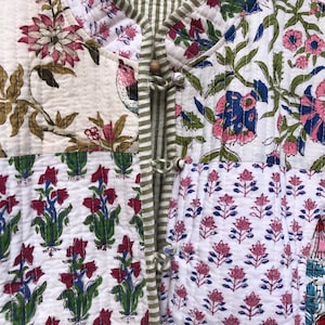 Op de afbeelding: Een wit gewatteerd jack met een bloemenprint. Het jack heeft een mandarijnskraag en een knoopsluiting. De stof is een patchwork van verschillende bloemenpatronen in tinten roze, blauw, groen en rood.