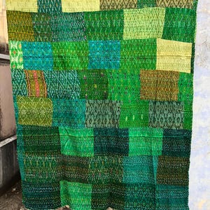 May include: A green kantha quilt with a patchwork design. The quilt is made of various shades of green fabric and is hand-stitched with a running stitch. The quilt is a traditional Indian textile and is often used as a bedspread or throw.