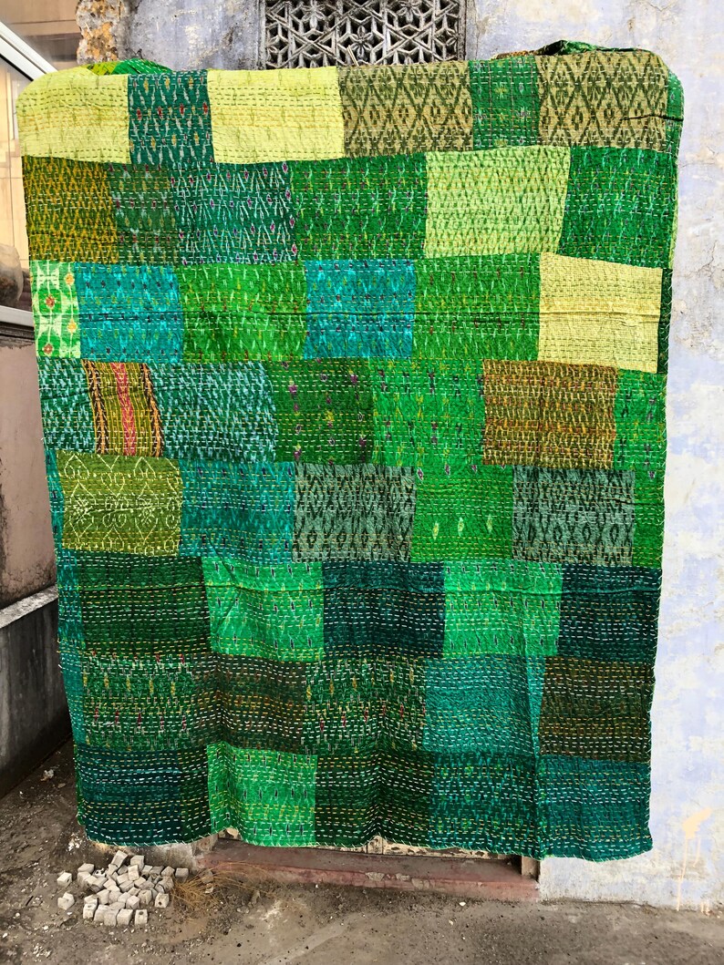 May include: A green kantha quilt with a patchwork design. The quilt is made of various shades of green fabric and is hand-stitched with a running stitch. The quilt is a traditional Indian textile and is often used as a bedspread or throw.