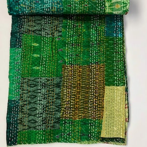 Puede incluir: Una colcha kantha verde con un diseño de patchwork. La colcha está hecha de varios tonos de verde y marrón y está cosida a mano con intrincados patrones.