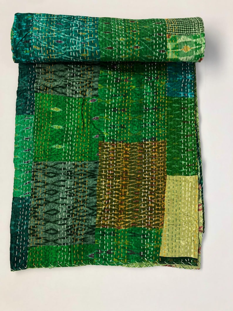 May include: A green kantha quilt with a patchwork design. The quilt is made of various shades of green and brown fabric and is hand-stitched with intricate patterns.