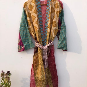 May include: A multi-colored silk robe with a patchwork design. The robe has a tie belt and is hanging on a wooden hanger. The tag on the robe says "NK-675".