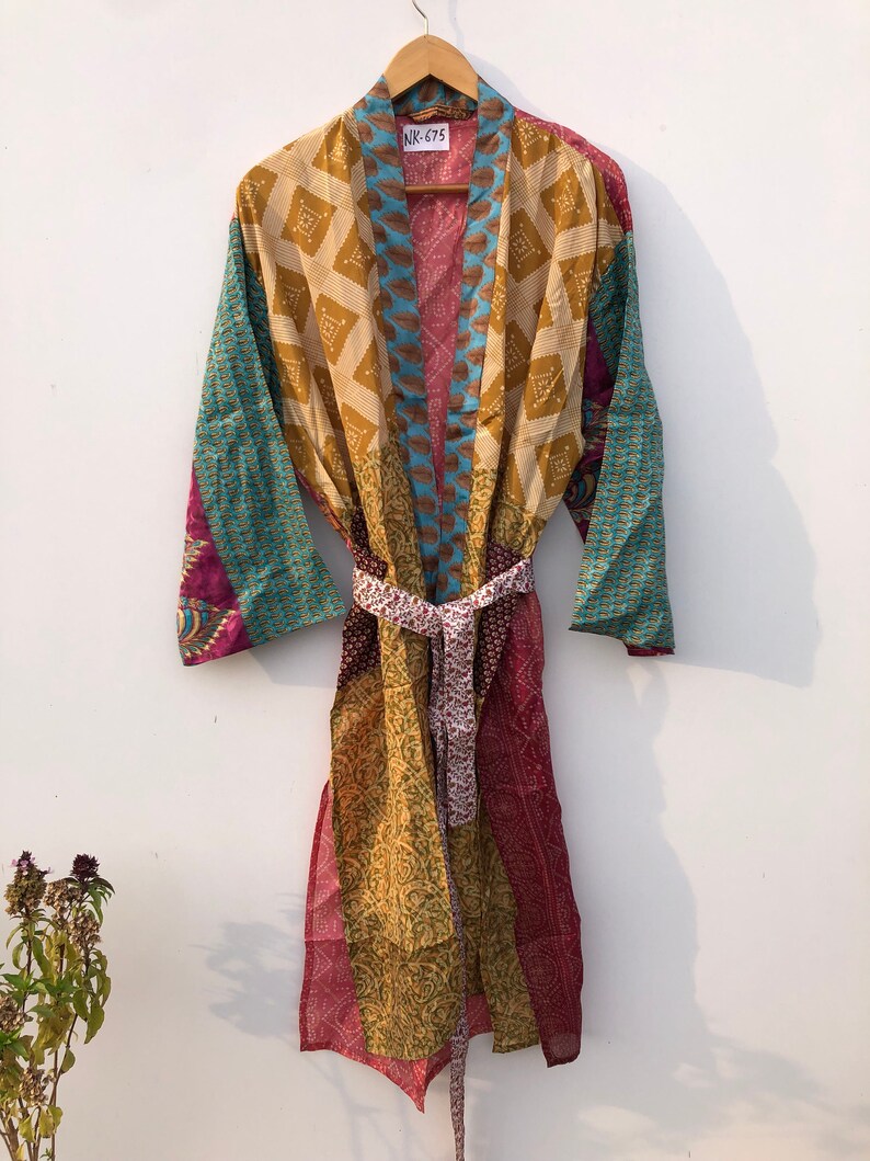 May include: A multi-colored silk robe with a patchwork design. The robe has a tie belt and is hanging on a wooden hanger. The tag on the robe says "NK-675".