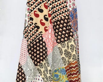 Puede incluir: Una falda larga de patchwork con una variedad de patrones y colores. La falda presenta diseños de cachemira, florales y geométricos en tonos de rojo, negro, beige, rosa y azul. La falda se muestra en un maniquí.