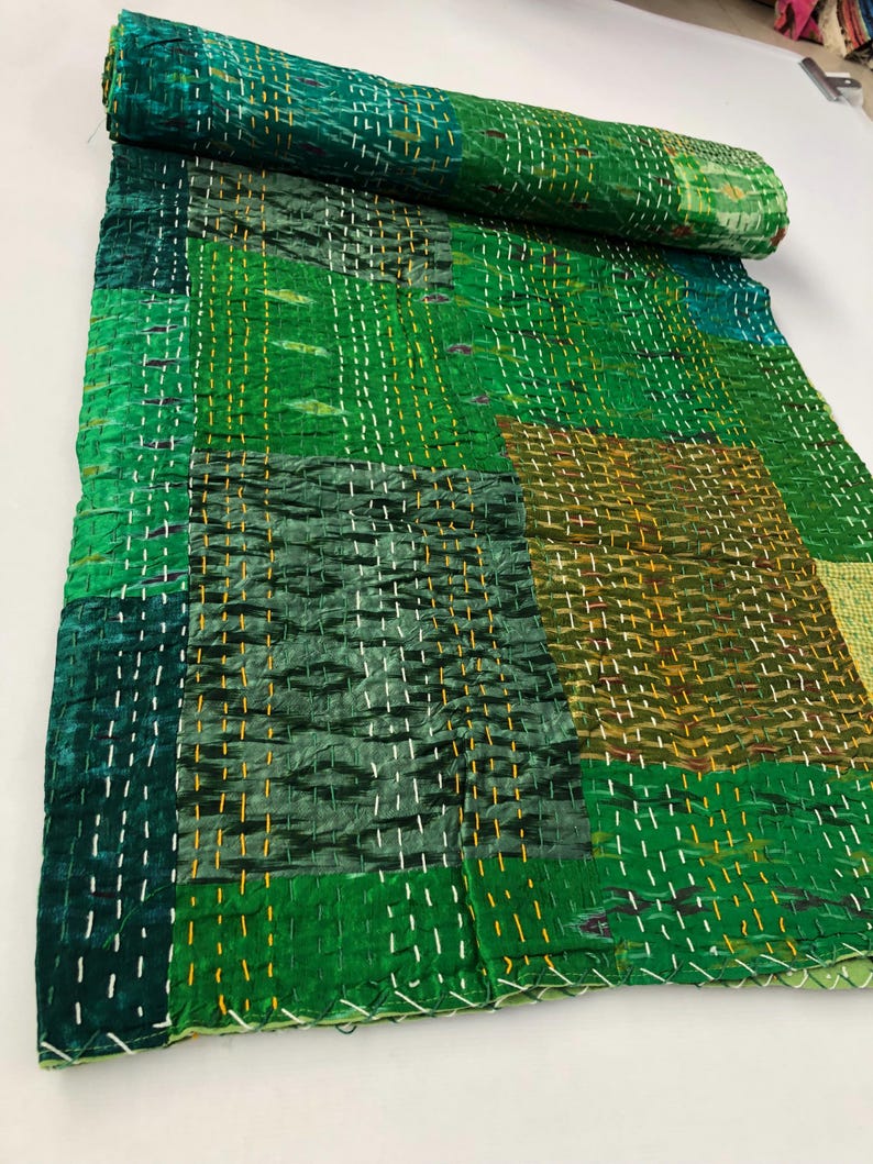 May include: A green kantha quilt with a patchwork design. The quilt is made of recycled saris and is hand-stitched with a running stitch. The quilt is perfect for adding a touch of bohemian style to your home.