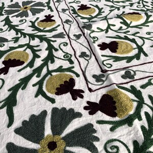 May include: White fabric with intricate embroidery in shades of green, yellow, and burgundy. The design features stylized flowers and leaves.