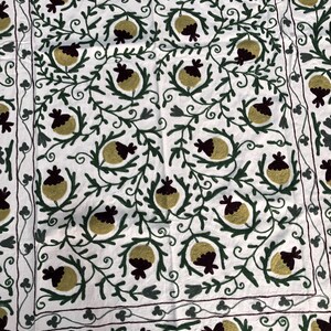 May include: White fabric with intricate embroidery of green vines and yellow and burgundy pomegranates.