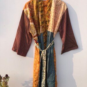 May include: A long, patchwork robe with a tie belt. The robe is made of different fabrics in shades of brown, orange, and blue. The fabric has floral and geometric patterns. The robe has a label that says "NK-631".