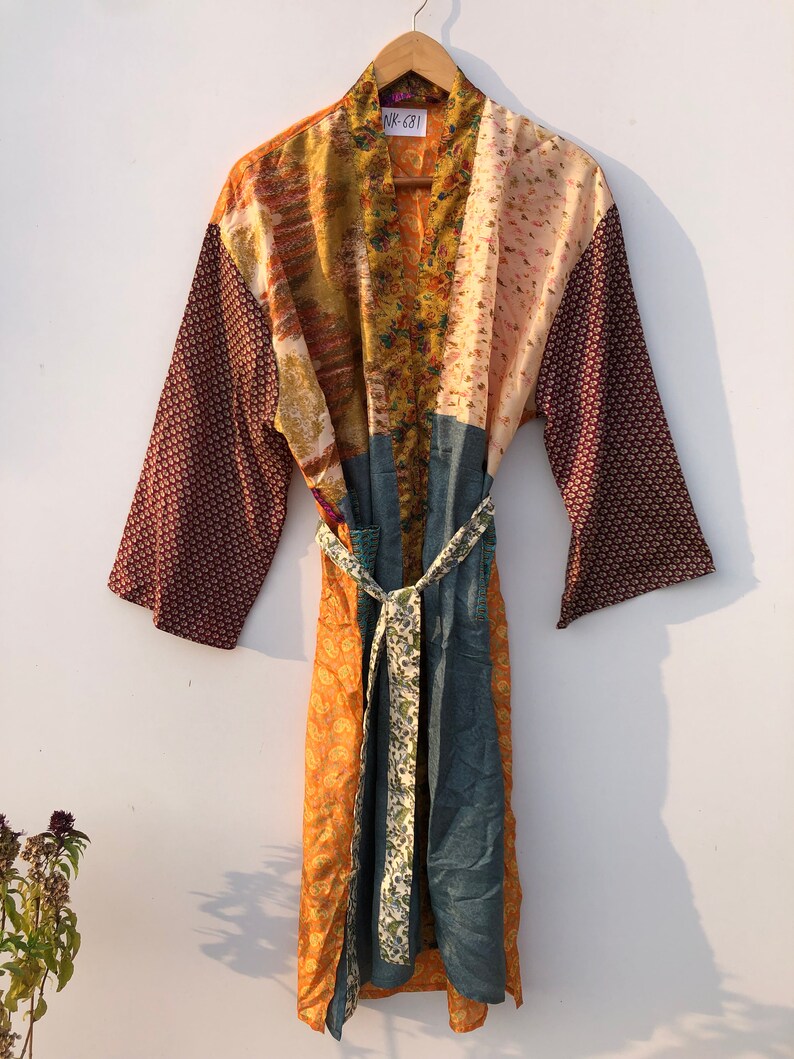 May include: A long, patchwork robe with a tie belt. The robe is made of different fabrics in shades of brown, orange, and blue. The fabric has floral and geometric patterns. The robe has a label that says "NK-631".