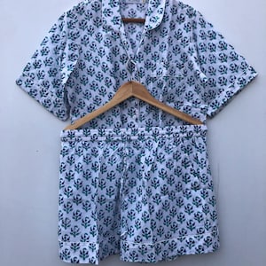 Puede incluir: Un conjunto de pijama blanco con estampado floral azul y verde. La parte superior tiene mangas cortas y cuello. Los pantalones cortos tienen una cintura elástica.