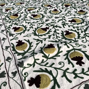 May include: White cotton fabric with a repeating pattern of green embroidered vines and yellow and burgundy embroidered flowers.