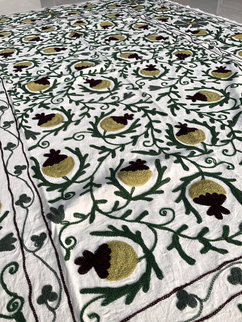 May include: White cotton fabric with a repeating pattern of green embroidered vines and yellow and burgundy embroidered flowers.
