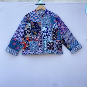 Op de afbeelding: Een blauw en wit patchwork jack met een bloemenprint. Het jack heeft een mandarijnsluiting en lange mouwen.
