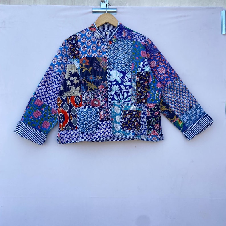 Op de afbeelding: Een blauw en wit patchwork jack met een bloemenprint. Het jack heeft een mandarijnsluiting en lange mouwen.