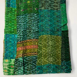 May include: A green kantha quilt with a patchwork design. The quilt is made of recycled saris and is hand-stitched. It features a variety of green shades and a few yellow and red accents.