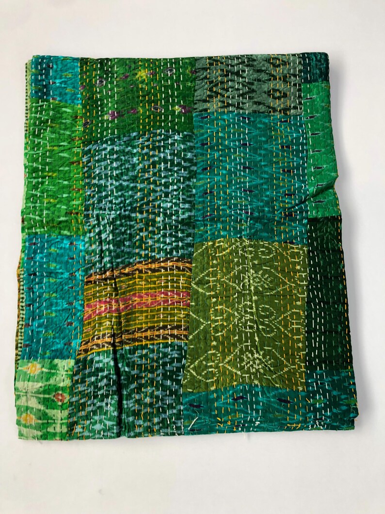 May include: A green kantha quilt with a patchwork design. The quilt is made of recycled saris and is hand-stitched. It features a variety of green shades and a few yellow and red accents.