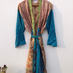May include: A long, colorful silk robe with a paisley print. The robe has a green, blue, and brown patchwork design. The robe is tied with a matching sash. The tag on the robe reads "NK677".