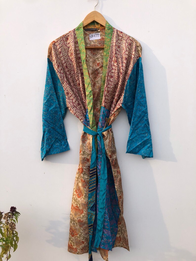 May include: A long, colorful silk robe with a paisley print. The robe has a green, blue, and brown patchwork design. The robe is tied with a matching sash. The tag on the robe reads "NK677".