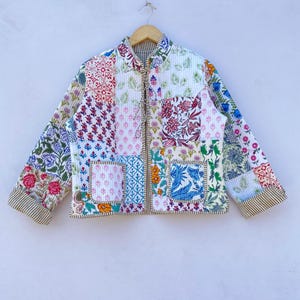 May include: A white quilted jacket with a patchwork design featuring various floral patterns in shades of pink, blue, green, and red. The jacket has a zipper closure and a mandarin collar.