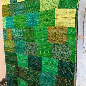 May include: A patchwork quilt made from various shades of green fabric. The quilt is made up of squares and rectangles of different sizes and patterns. The quilt is hanging on a wall.