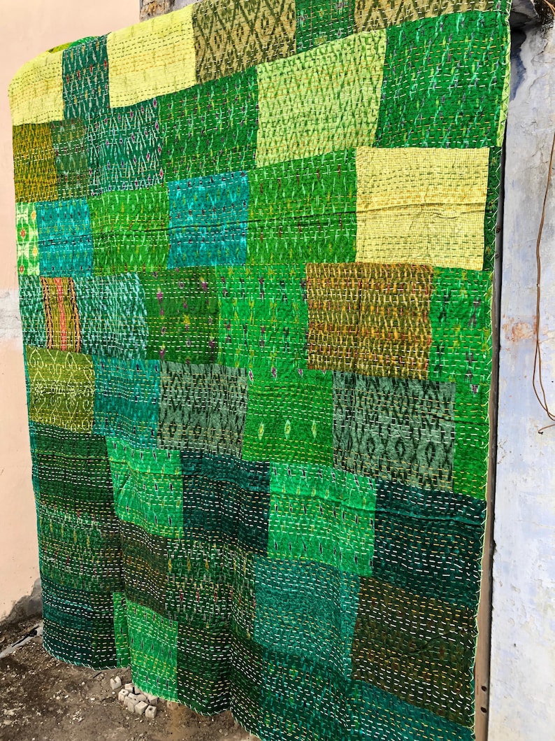 May include: A patchwork quilt made from various shades of green fabric. The quilt is made up of squares and rectangles of different sizes and patterns. The quilt is hanging on a wall.