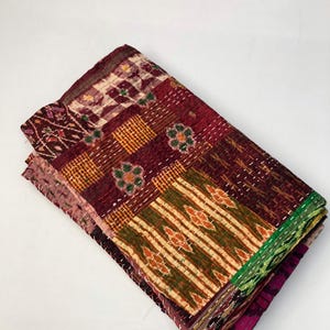 May include: A patchwork quilt made from various fabrics in shades of burgundy, green, and gold. The quilt is hand-stitched and has a unique, rustic look.