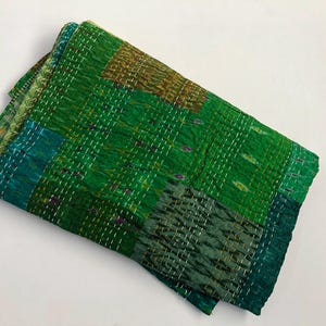May include: A green kantha quilt with a patchwork design. The quilt is made of recycled saris and is hand-stitched. It is a traditional Indian textile.