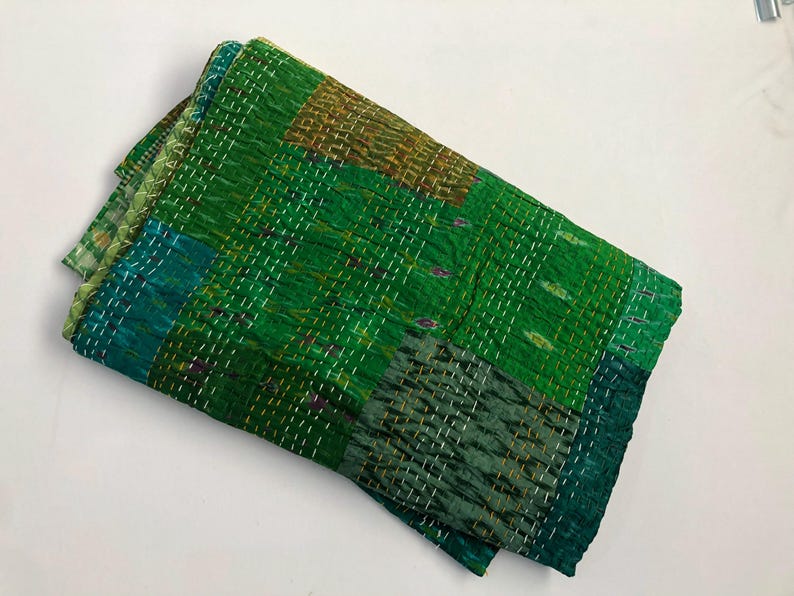May include: A green kantha quilt with a patchwork design. The quilt is made of recycled saris and is hand-stitched. It is a traditional Indian textile.