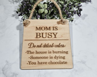 May include: A wooden sign with the text "MOM IS BUSY Do not disturb unless: -The house is burning -Someone is dying -You have chocolate" hanging from a twine rope.