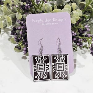 May include: A pair of silver earrings with a black and white circuit board design. The earrings are on a purple card with the text "Purple Jen Designs Uniquely yours".