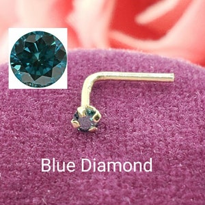 Könnte beinhalten: Ein goldener Nasenring mit einem blauen Diamanten. Der Diamant ist rund und hat einen facettierten Schliff. Der Ring ist in einem 90-Grad-Winkel gebogen. Blauer Diamant.