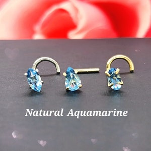 May include: Three nose rings with a teardrop shaped aquamarine gemstone. The rings are made of silver and gold.